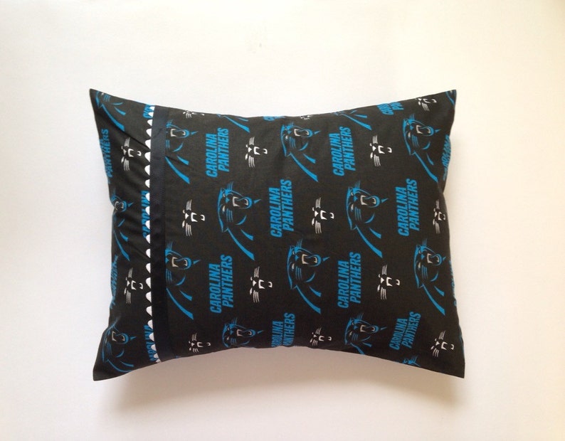 Puede incluir: Una almohada negra y azul con un patr&oacute;n repetido de logotipos de los Carolina Panthers. La almohada tiene un ribete blanco y negro.