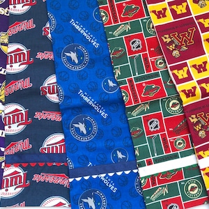 May include: A collection of five fabric swatches featuring different Minnesota sports team logos. The swatches are in various colours, including purple, blue, red, green, and yellow. The logos include the Minnesota Vikings, Minnesota Timberwolves, Minnesota Wild, and the University of Minnesota Golden Gophers.