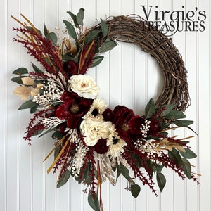 May include: A burgundy and cream floral wreath with a grapevine base. The wreath features burgundy velvet flowers, cream roses, and dried grasses.