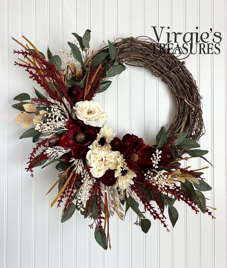 May include: A burgundy and cream floral wreath with a grapevine base. The wreath features burgundy velvet flowers, cream roses, and dried grasses.