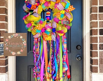 Könnte beinhalten: Ein bunter Cinco de Mayo-Kranz mit gelbem, rosa, grünem, blauem und orangefarbenem Netz und Bändern. Der Kranz ist mit einer Piñata, einem Sombrero und einem kleinen Haus verziert. Der Kranz hängt an einer schwarzen Tür mit einem Schild, auf dem "Virgie's Treasures" steht.