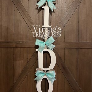 May include: White wooden letters spelling "I DO" with turquoise bows attached to each letter. The letters are hanging on a wooden door.