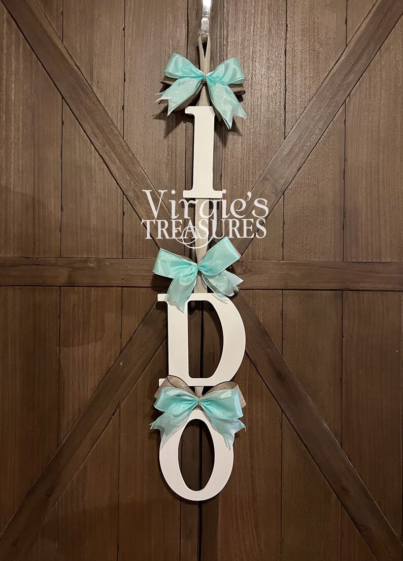 May include: White wooden letters spelling "I DO" with turquoise bows attached to each letter. The letters are hanging on a wooden door.