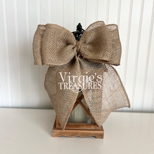 May include: A wooden lantern with a burlap bow on top. The lantern has a clear glass panel and a wooden base. The text "Virgie's Treasures" is visible on the lantern.