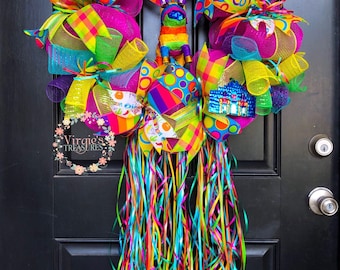 Könnte beinhalten: Ein bunter Cinco de Mayo-Kranz mit einer Piñata, einem Sombrero und Bändern. Der Kranz ist mit leuchtenden Farben verziert, darunter Pink, Grün, Gelb, Blau und Orange. Der Kranz hängt an einer schwarzen Tür.