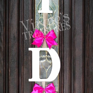 May include: White wooden letters spelling "I DO" with pink bows hanging on a dark brown wooden door.