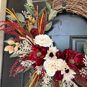 May include: A burgundy and cream floral wreath with a grapevine base. The wreath features burgundy velvet flowers, cream roses, and eucalyptus leaves.