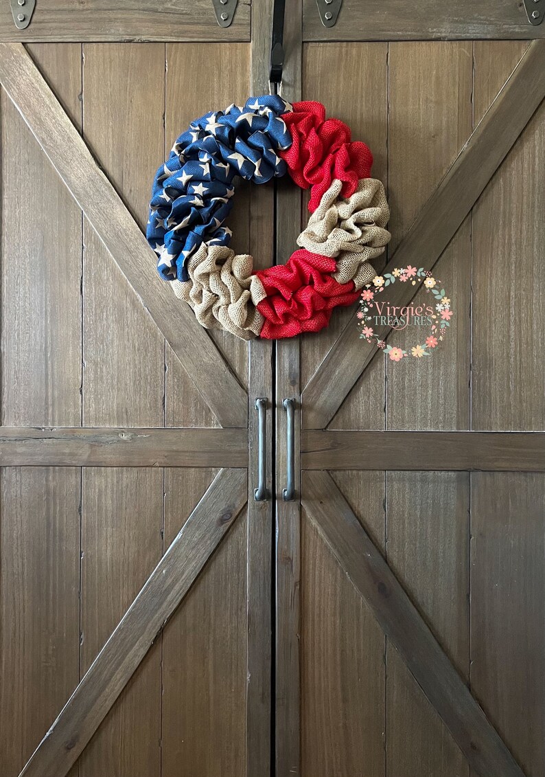 Puede incluir: Una corona de arpillera roja, blanca y azul con un patr&oacute;n de estrellas en la secci&oacute;n azul. La corona est&aacute; colgada en una puerta de madera con un acabado r&uacute;stico.