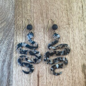 May include: A pair of black and white snake-shaped earrings with gold hooks and black lava rock beads.