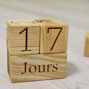 Puede incluir: Bloques de madera que deletrean "17 Jours" con un bloque separado con el número "2" en él. Los bloques son de madera clara con un acabado natural.
