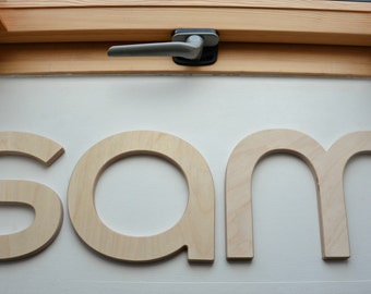 May include: Wooden letters spelling out the name "sam" in a light brown color. The letters are cut out and have a simple, modern design.