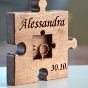 May include: A wooden puzzle piece shaped ring box with the name "Alessandra" and the date "30.10." engraved on it. The box has a cutout for a ring.