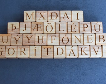 May include: Wooden blocks with letters of the alphabet, including some with accents, arranged in a pyramid shape on a gray surface. The letters spell out "MXDAI BJAEÖLEPÜ UYYH FÖNEB GORÍT DÁKVS".