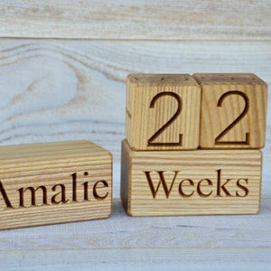 May include: Wooden blocks spelling out "Amalie" and "22 Weeks". The blocks are made of natural wood and have a rustic look.