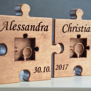 May include: A wooden puzzle ring holder with two pieces, one with the name "Alessandra" and the other with the name "Christian". The date "30.10. 2017" is engraved on the bottom of the holder.