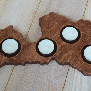 May include: A wooden candle holder shaped like the outline of Latvia, with four circular cutouts for tealight candles.