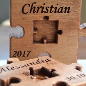 May include: Two wooden puzzle pieces with the names "Christian" and "Alessandra" engraved on them. The pieces are joined together and have the date "2017 30.10" engraved on them.