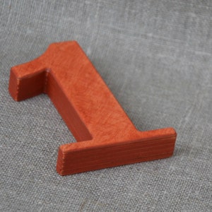 Op de afbeelding: Een houten nummer &eacute;&eacute;n, geverfd in een heldere oranje-rode kleur. Het nummer is gemaakt van massief hout en heeft een glad, licht getextureerd oppervlak.