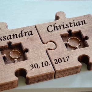 May include: A wooden puzzle ring holder with two pieces, one with the name "Alessandra" and the other with the name "Christian". The date "30.10.2017" is engraved on the bottom piece.