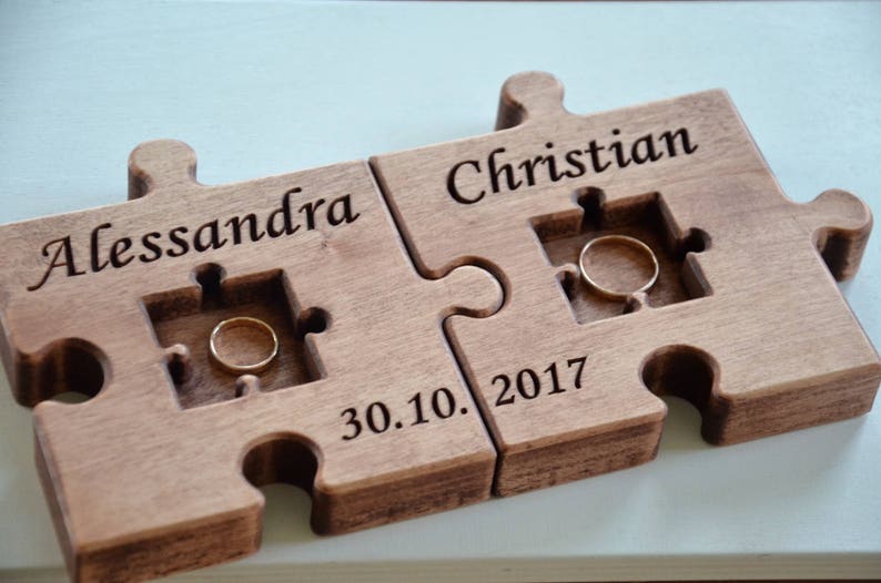 May include: A wooden puzzle ring holder with two pieces, one with the name "Alessandra" and the other with the name "Christian". The date "30.10.2017" is engraved on the bottom piece.
