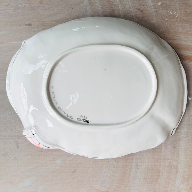 May include: White ceramic serving dish with a scalloped edge. The bottom of the dish is marked "Bordighera" and "Fatto a Mano in Italia".