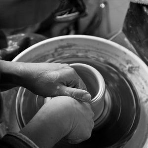 May include: A person's hands shaping a clay pot on a pottery wheel. The wheel is spinning and the clay is being molded into a round shape.