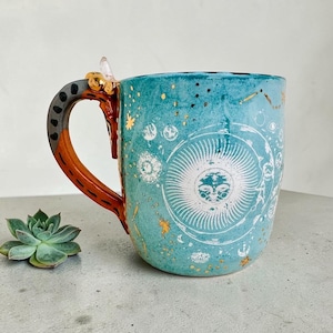 Puede incluir: Una taza de cerámica blanca con un asa negra y el texto "But First, Coffee" en negro, con una fuente de estilo manuscrito. La taza está sobre una superficie blanca.