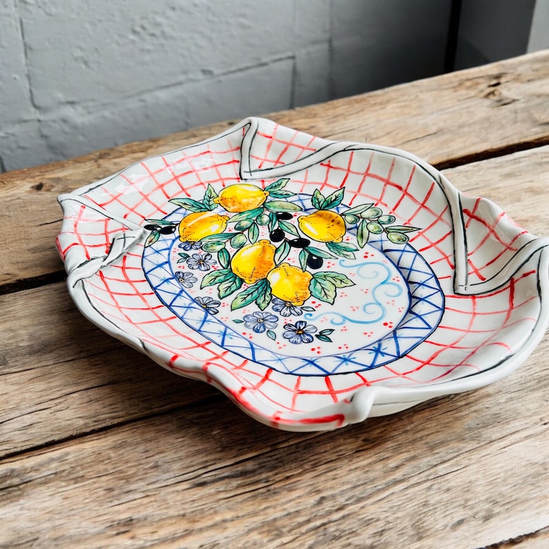 May include: White ceramic serving platter with a red and blue checkered pattern and a painted design of lemons and olives on a branch.