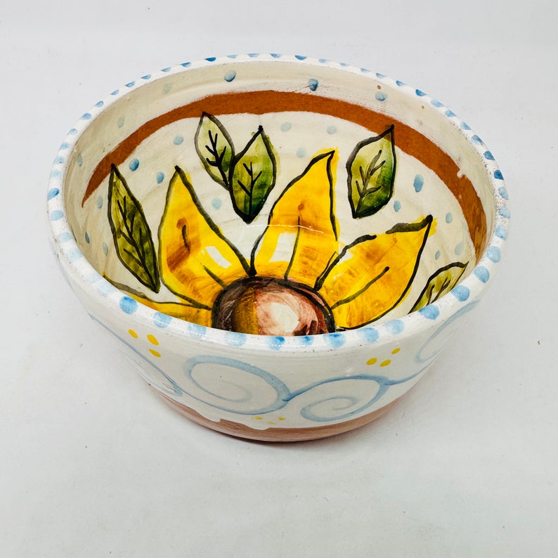 May include: A white ceramic bowl with a blue and yellow sunflower design. The bowl has a brown rim and a white interior.