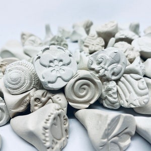 May include: A collection of white ceramic stamps with various designs, including a flower, a spiral, and a shell. The stamps are perfect for adding unique details to crafts and projects.