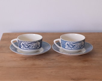 Puede incluir: Dos tazas de té azules y blancas con un patrón floral. Las tazas y los platillos están sobre una mesa de madera.