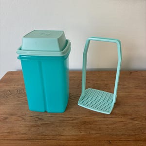 May include: A vintage turquoise plastic container with a matching lid and a separate turquoise potato masher. The container is rectangular with a light blue lid. The potato masher has a perforated base and a handle.