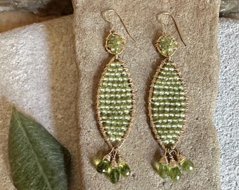 May include: A pair of long, green gemstone earrings with gold wire wrapping. The earrings feature a teardrop shape with a cluster of smaller gemstones at the bottom.