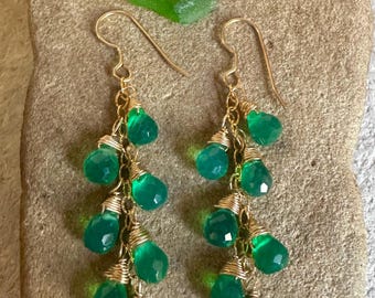 Puede incluir: Un par de pendientes colgantes con múltiples cuentas verdes facetadas en forma de lágrima suspendidas de cadenas de alambre dorado. Cada cuenta está envuelta individualmente en un hilo de oro fino, creando un diseño de racimo en cascada.