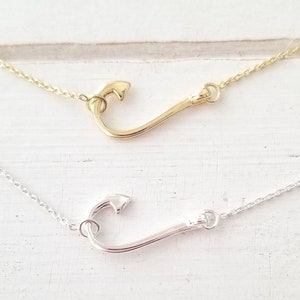 May include: Two delicate necklaces with a fish hook pendant. The top necklace has a gold-toned hook, while the bottom necklace has a silver-toned hook.
