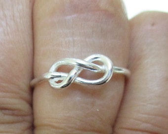May include: A silver knot ring worn on a finger.
