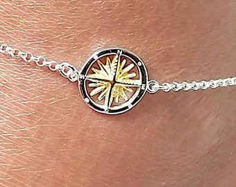 May include: Silver ankle bracelet with a delicate chain and a round charm featuring a gold compass design.