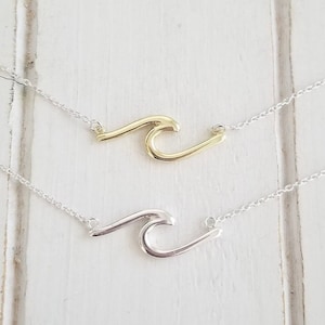 May include: Two delicate necklaces with wave pendant charms. One necklace features a gold wave charm, while the other features a silver wave charm.