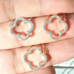 Puede incluir: Dos collares de oro con un colgante de tr&eacute;bol de cuatro hojas engastado con piedras de circonita c&uacute;bica transparentes. Los collares est&aacute;n en una mano.