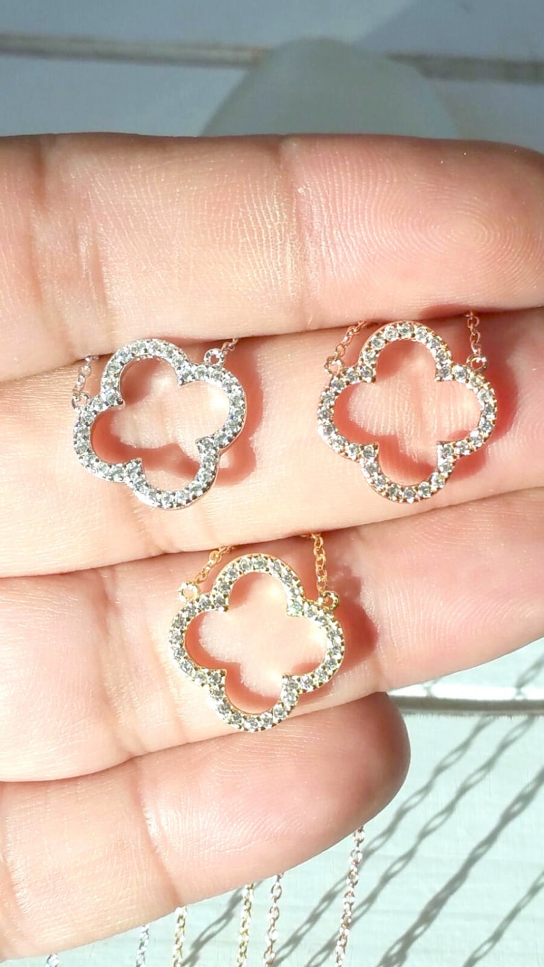 Puede incluir: Dos collares de oro con un colgante de tr&eacute;bol de cuatro hojas engastado con piedras de circonita c&uacute;bica transparentes. Los collares est&aacute;n en una mano.