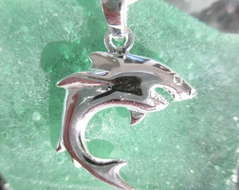 May include: A silver shark pendant necklace. The shark is in a jumping pose with its mouth open. The pendant is on a green background.