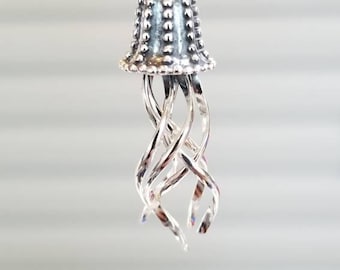 May include: A silver charm in the shape of a jellyfish with a textured bell and curled tentacles.