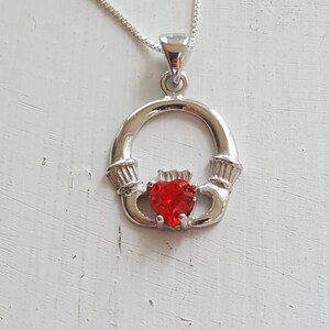 May include: A silver Celtic knot pendant necklace with a red heart-shaped gemstone in the center.