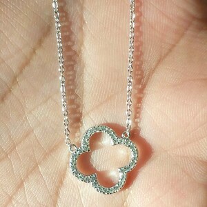 Puede incluir: Un collar de cadena de plata con un colgante de tr&eacute;bol de cuatro hojas incrustado con peque&ntilde;as piedras transparentes.