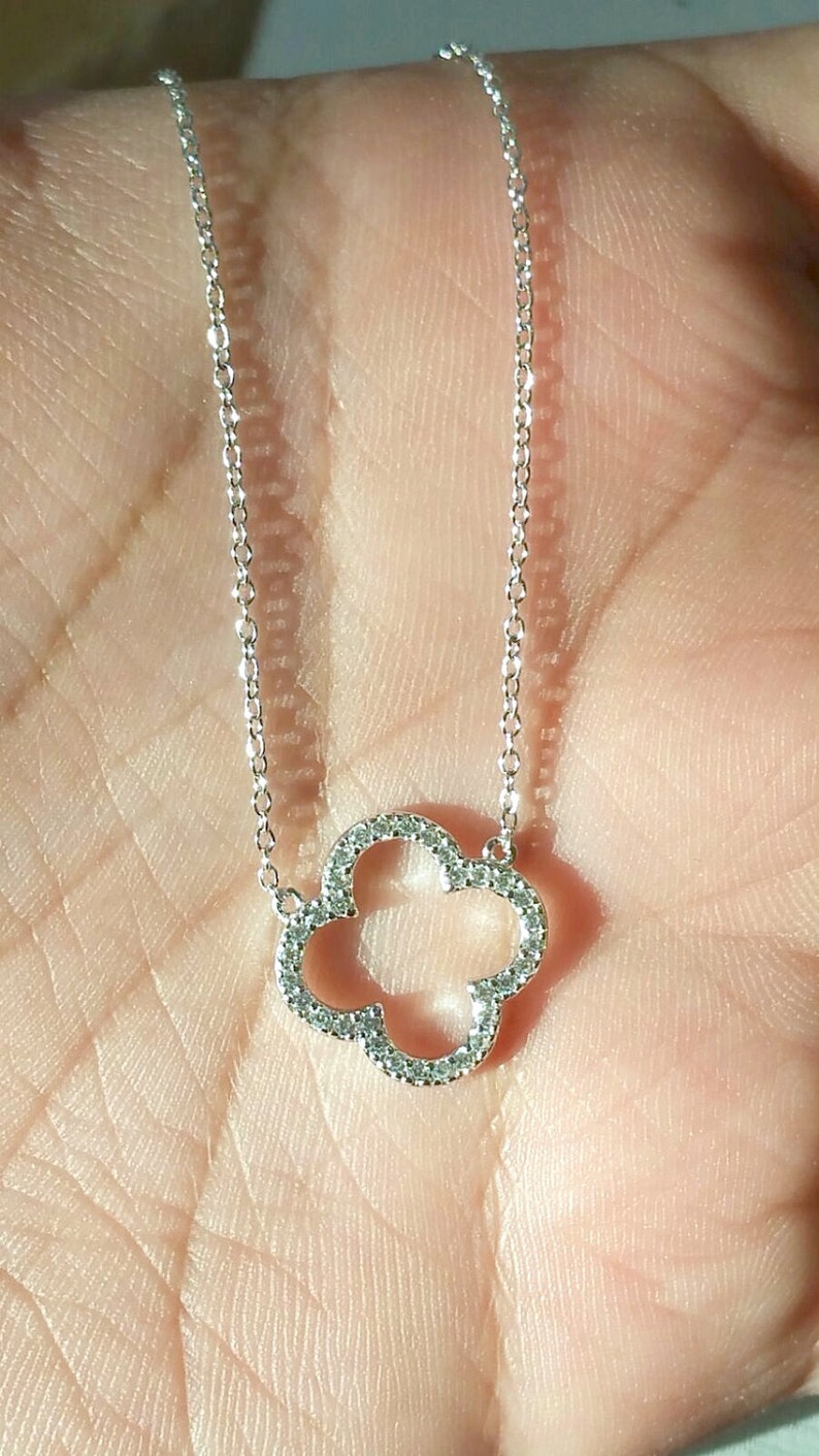 Puede incluir: Un collar de cadena de plata con un colgante de tr&eacute;bol de cuatro hojas incrustado con peque&ntilde;as piedras transparentes.