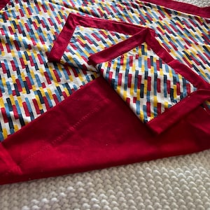 May include: A set of three red placemats with a geometric pattern of yellow, blue, and gray stripes. The placemats are folded on top of each other.