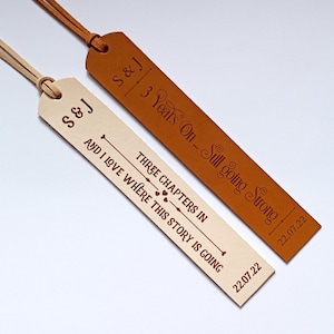 May include: Two rectangular leather bookmarks with suede cords. The light beige bookmark features the text S&J, THREE CHAPTERS IN, AND I LOVE WHERE THIS STORY IS GOING, and 22.07.22. The brown bookmark features S&J, 3 Years On... Still going Strong, and 22.07.22.