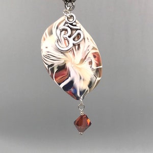May include: A silver chain necklace with a white, red, and blue swirl glass pendant. The pendant has a silver Om symbol charm and a red crystal dangle.