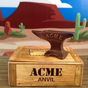 May include: A brown metal anvil with the word "ACME" embossed on the top. The anvil is sitting on a wooden crate with the words "ACME ANVIL" printed on the front.