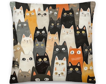 May include: A square throw pillow featuring a dense, repeating pattern of illustrated cats in various colors including black, white, orange, and gray. Each cat has distinct facial features, wide eyes, and whiskers, covering the entire surface.